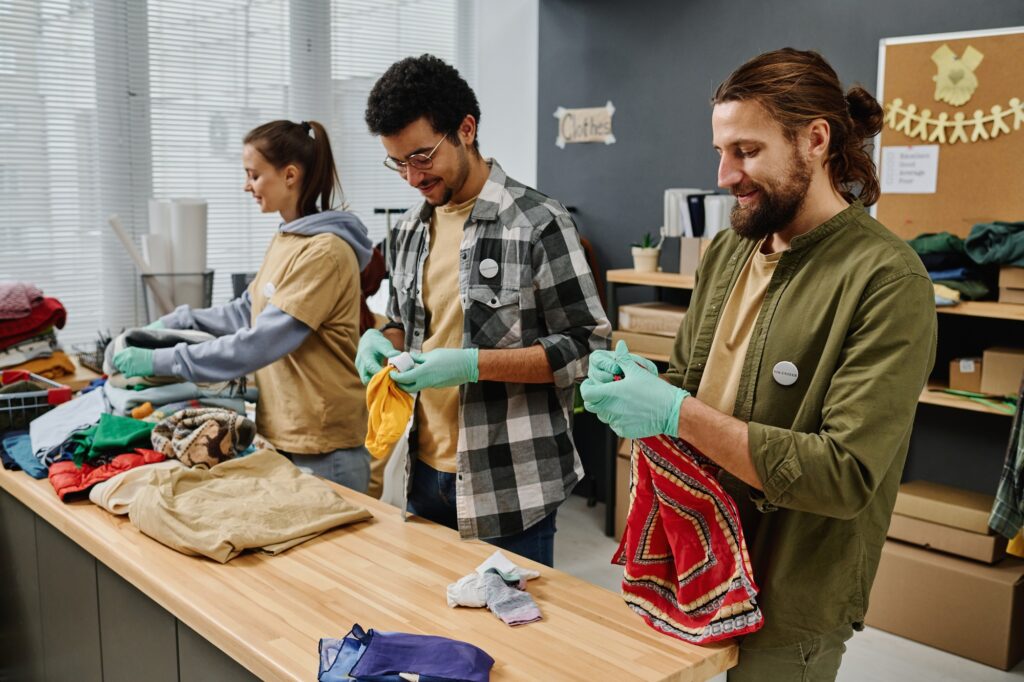 Row of young intercultural people sorting second hand clothes
